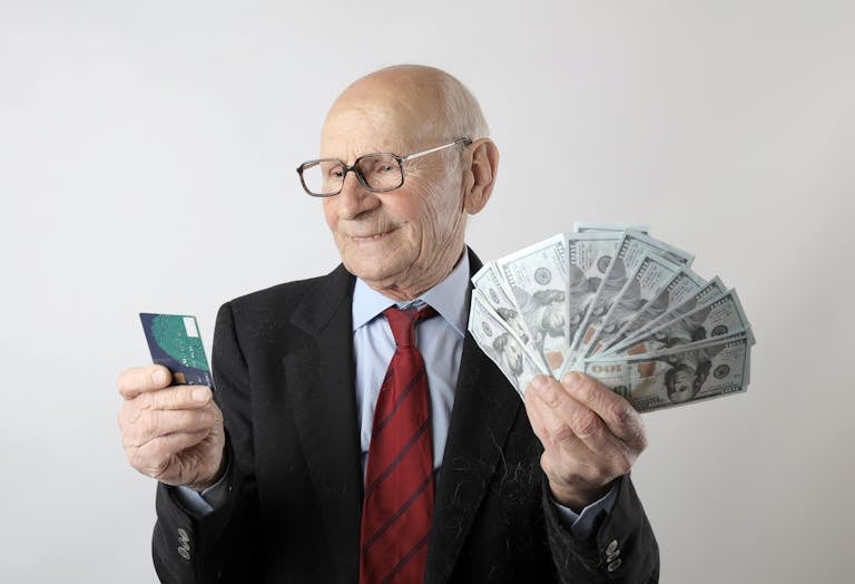 Elderly man in a suit holding a credit card and US dollar bills, representing finance and wealth.